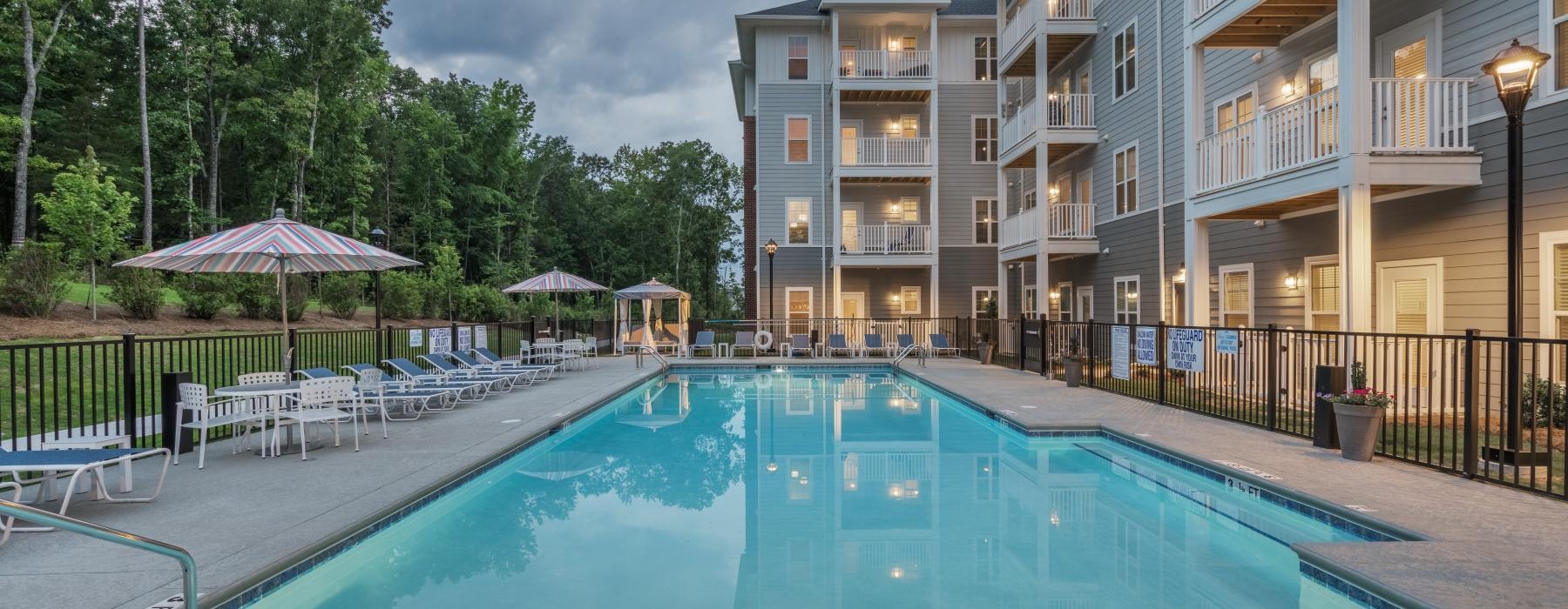 The pool area at Arden at Indian Land Apartments in South Carolina, featuring lounge chairs and umbrellas.